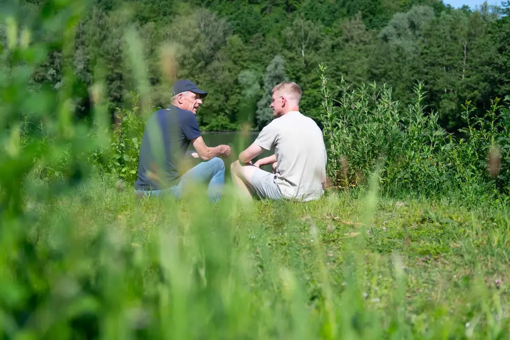 Peter Vos in gesprek met een jongeman, samen zittend in het gras in de natuur