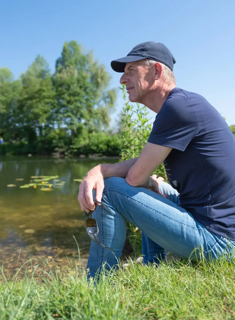 Peter Vos zit in het gras aan de waterkant en kijkt rustig voor zich uit
